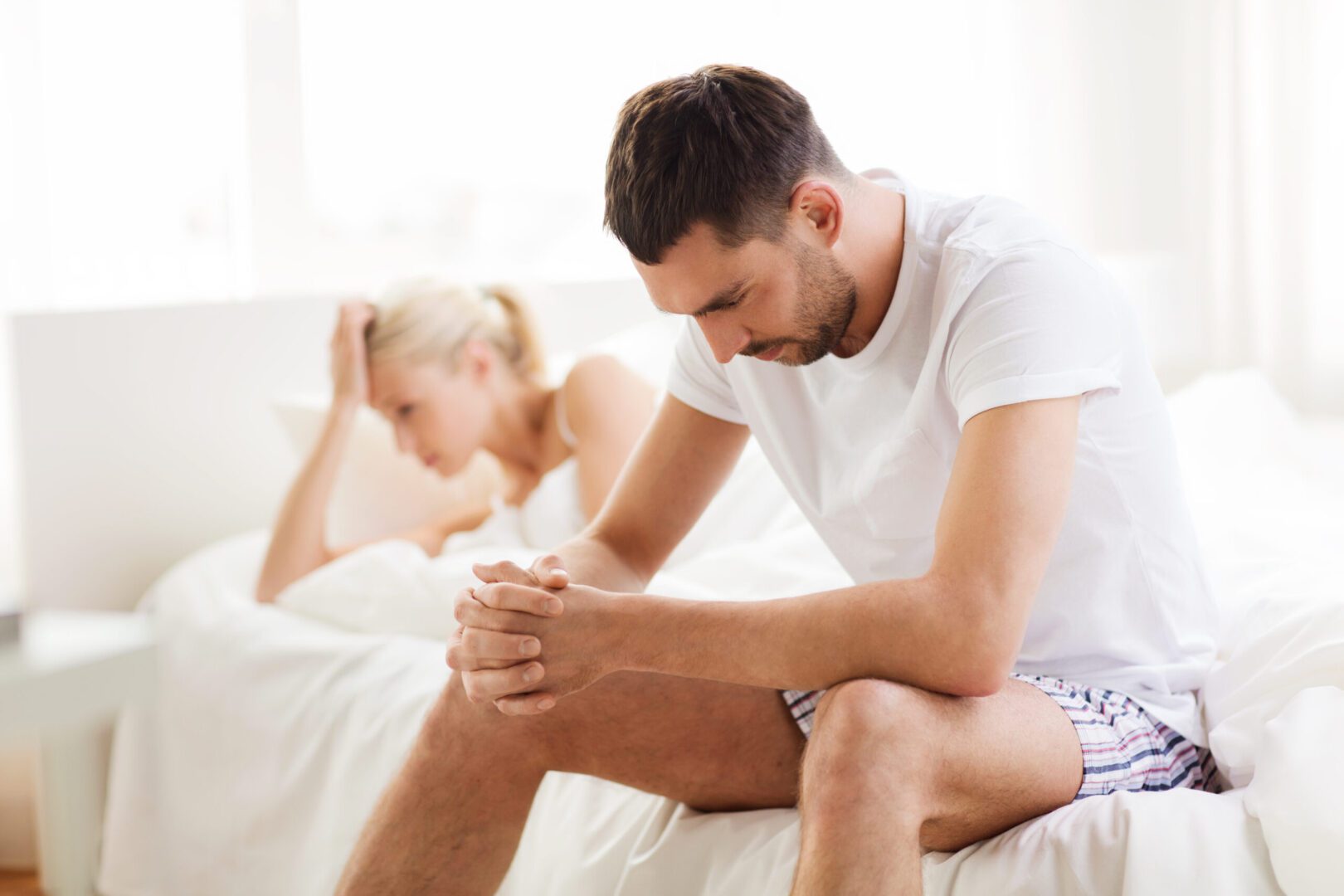 a man worried about low testosterone sitting on a bed with a woman in the background